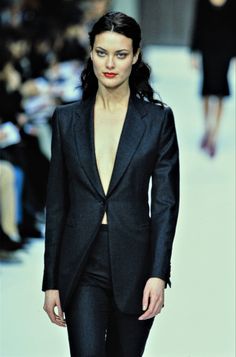 a woman walking down a runway wearing a black suit and red lipstick on her lips