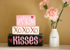 pink carnations in a vase next to two valentine's day boxes on a shelf