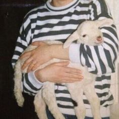 a man holding a baby lamb in his arms while wearing jail clothes and looking at the camera