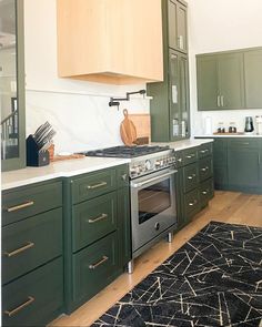 a kitchen with green cabinets and an oven in the center, along with a black rug on the floor