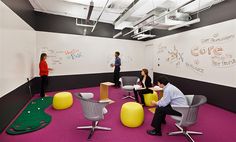 three people are in an office setting with colorful chairs and chalkboards on the wall