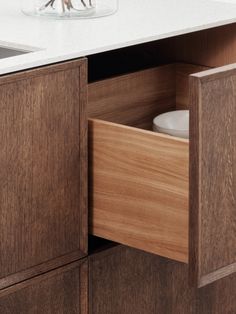 an open drawer in a kitchen next to a sink and counter top with a glass vase filled with flowers