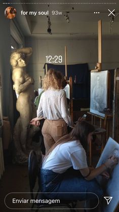 two women are sitting in front of an easel and some art work on display