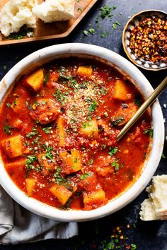 a white bowl filled with stew next to bread