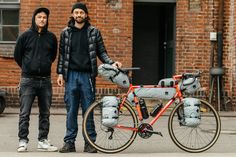 two men standing next to a bike with luggage strapped on the front and back wheels