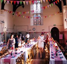 many people are standing around tables with food on them and flags hanging from the ceiling