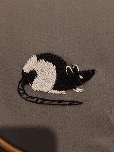 a black and white rat embroidered onto a gray shirt with a brown leather chair handle