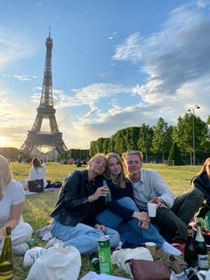 three people sitting on the grass in front of the eiffel tower