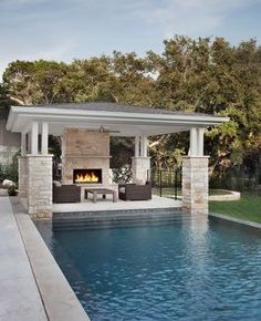 an outdoor living area next to a swimming pool and covered patio with fireplace in the middle