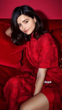 a woman in a red dress is sitting on a red couch and posing for the camera