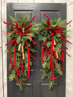 two christmas wreaths with bells and red ribbon hanging on the front door, decorated with greenery