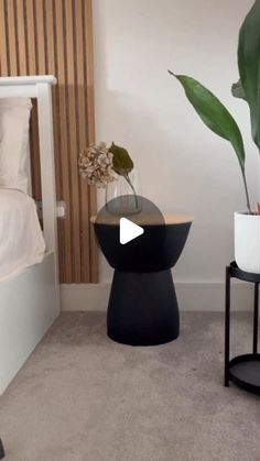 a bedroom with a bed, nightstand and plant on the side table in front of it