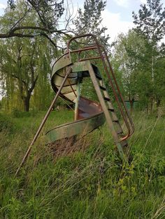 an old rusted metal boat sitting on top of a grass covered field next to trees