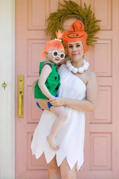 a woman holding a child in front of a pink door with wreaths on it