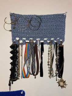 a crocheted blue wall hanging with lots of bracelets and eyeglasses attached to it