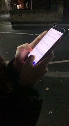 a person holding a cell phone in their hand on the street at night with lights on