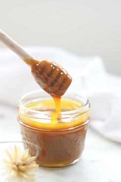 a honey dip being poured into a glass jar with a wooden spoon and flower on the side