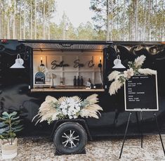 a black food truck parked in front of a forest filled with lots of trees and plants