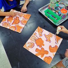 three children are sitting at a table making paper cut outs with scissors and glue on them