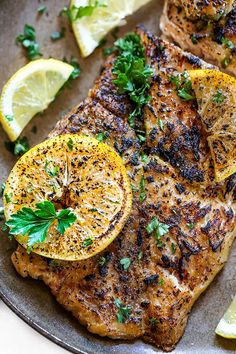 grilled pork chops with lemon and parsley on a plate next to lime wedges