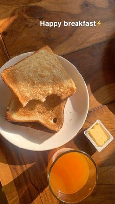 two pieces of toast on a white plate with butter and orange juice next to it