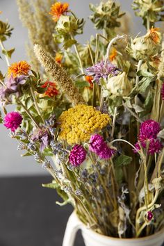 a white vase filled with lots of different colored wildflowers on top of a table