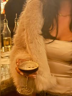 a woman is holding a wine glass in her hand and wearing a fur coat over her shoulders