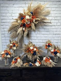 an arrangement of dried flowers and wheat stalks on a dresser in front of a brick wall