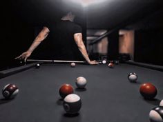 a man is playing pool in the dark with his arms extended and balls scattered around him