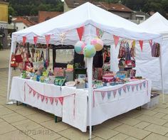 a white tent with balloons and other items on the table in front of it at an outdoor market