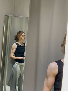 a man standing in front of a mirror looking at his reflection on the wall behind him