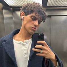 a man with curly hair is looking at his cell phone while standing in an elevator