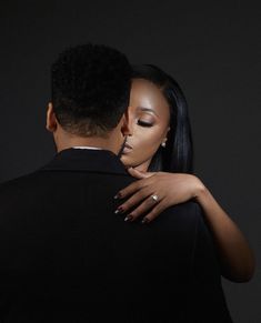 a man and woman embracing each other in front of a dark background with their eyes closed