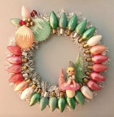 a wreath made out of shells and tinsels with a fairy figurine on top