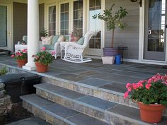 the front porch is decorated with flowers and rocking chairs for sitting on the steps to the patio