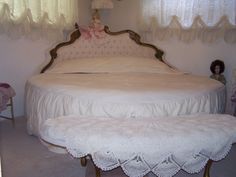 a white bed sitting in the middle of a bedroom next to a table with a doll on it