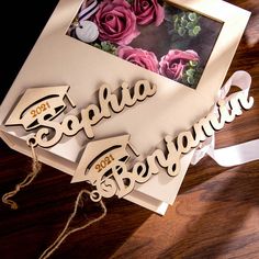 some type of wooden name sign on a table with flowers in the background and a ribbon around it