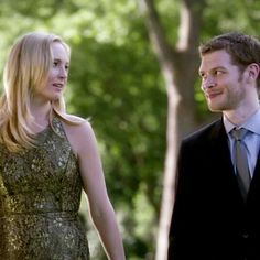 a man in a suit and tie standing next to a blonde woman wearing a dress