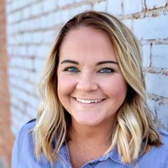 a woman smiling in front of a brick wall with blue eyeshadow and blonde hair