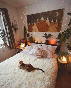 a cat laying on top of a white bed in a room with lights and plants