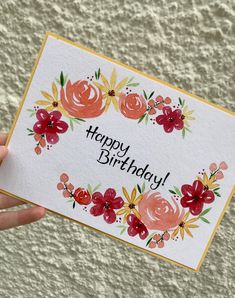 someone holding up a card with flowers on it that says happy birthday written in black ink