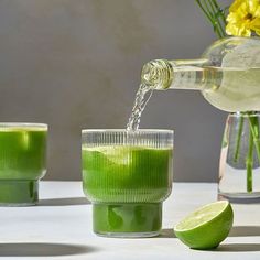 green liquid being poured into two glasses with limes and flowers in the back ground