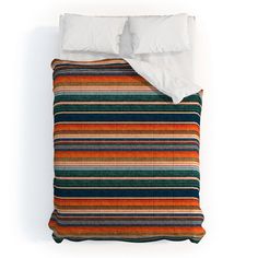 an orange, blue and green striped comforter on top of a bed with white pillows