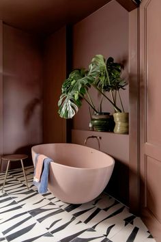 a bathroom with a pink bathtub and potted plant on the wall next to it