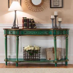 a green console table with flowers and books on it in front of two framed pictures