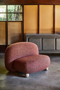 a red chair sitting on top of a cement floor next to a wooden dresser and window