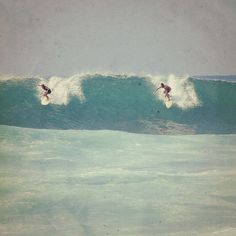 two surfers are riding the same wave in the ocean, one is on his surfboard