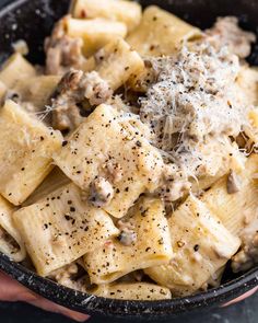 a black bowl filled with pasta and meat covered in cheese sprinkled on top