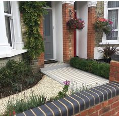 a brick house with flowers and plants growing on the front porch, along with a checkerboard walkway