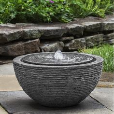 an outdoor fountain with water running from it's top to the bottom, surrounded by rocks and grass